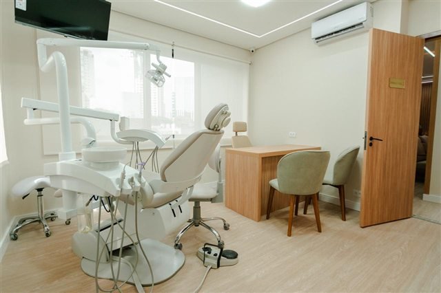Vista ampla do consultório odontológico com cadeira, bancada e iluminação natural